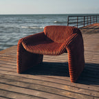Bough Chair in rust corduroy, seen from the front, with arms that carry down to the floor.